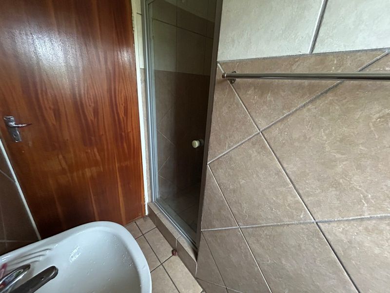 A functional bathroom featuring a shower enclosure, tiled walls and flooring, and a wash basin, presenting a dated but well-maintained space.