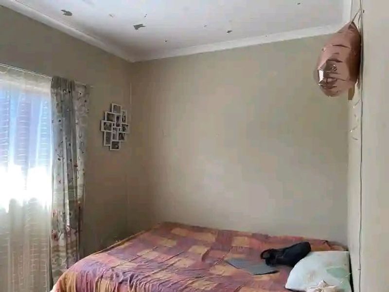 A bedroom featuring a window with curtains and visible ceiling paint deterioration requiring maintenance.