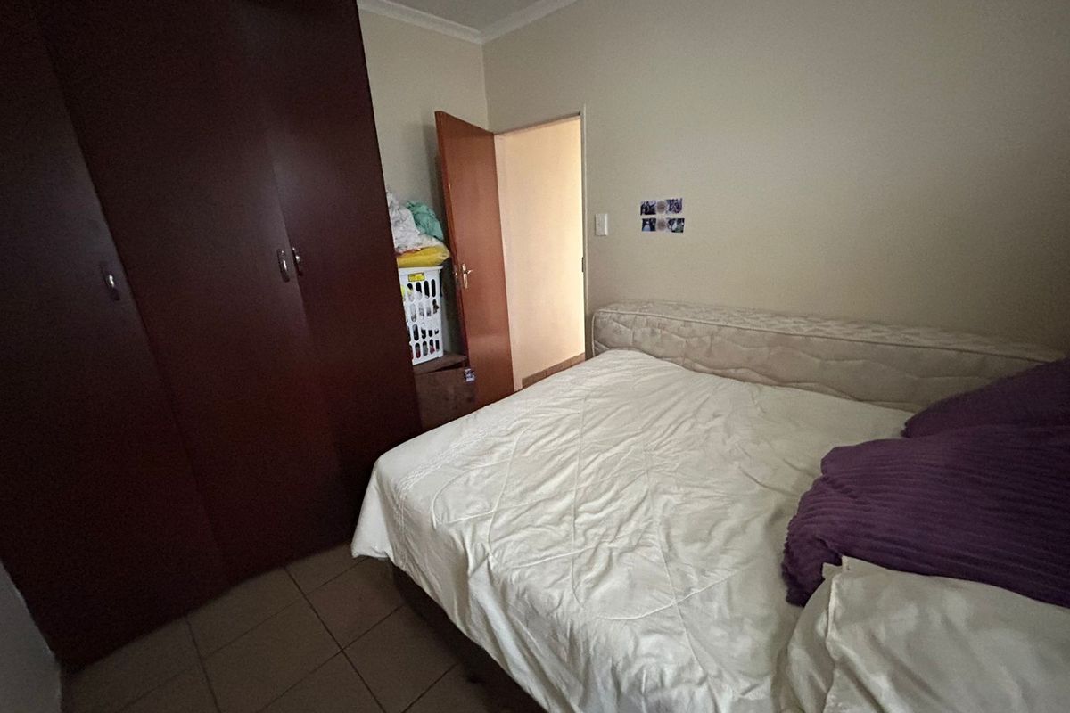 A functional bedroom featuring built-in wooden wardrobes and tiled flooring, providing a practical space with neutral wall finishes.