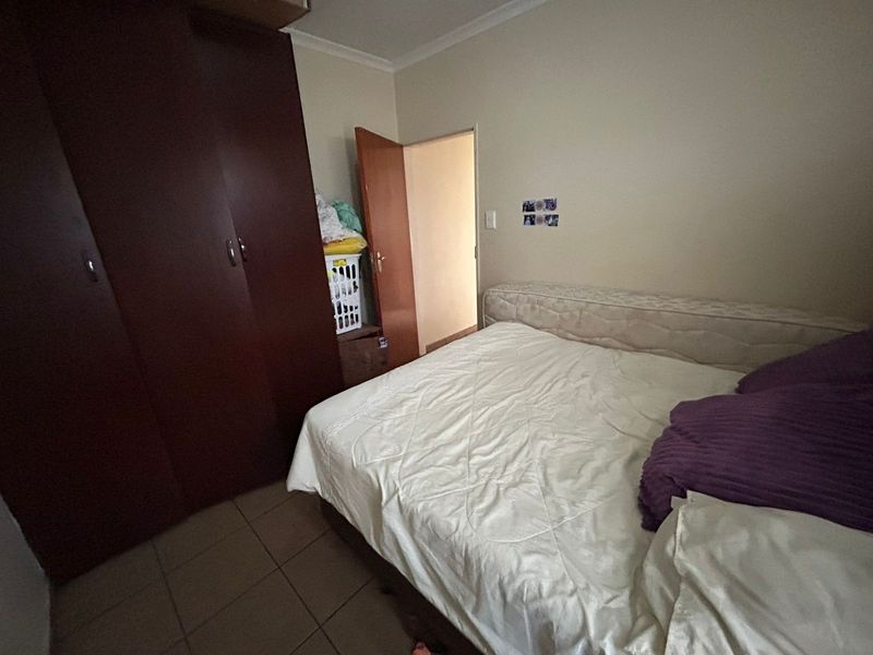 A functional bedroom featuring built-in wooden wardrobes and tiled flooring, providing a practical space with neutral wall finishes.
