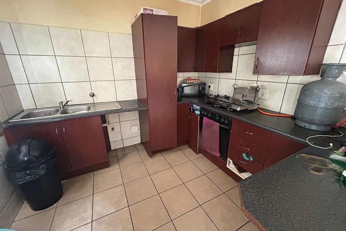 A functional kitchen featuring dark laminate cabinetry, tiled backsplash, built-in oven with gas hob, and ceramic floor tiles, offering potential for modern cosmetic updates.