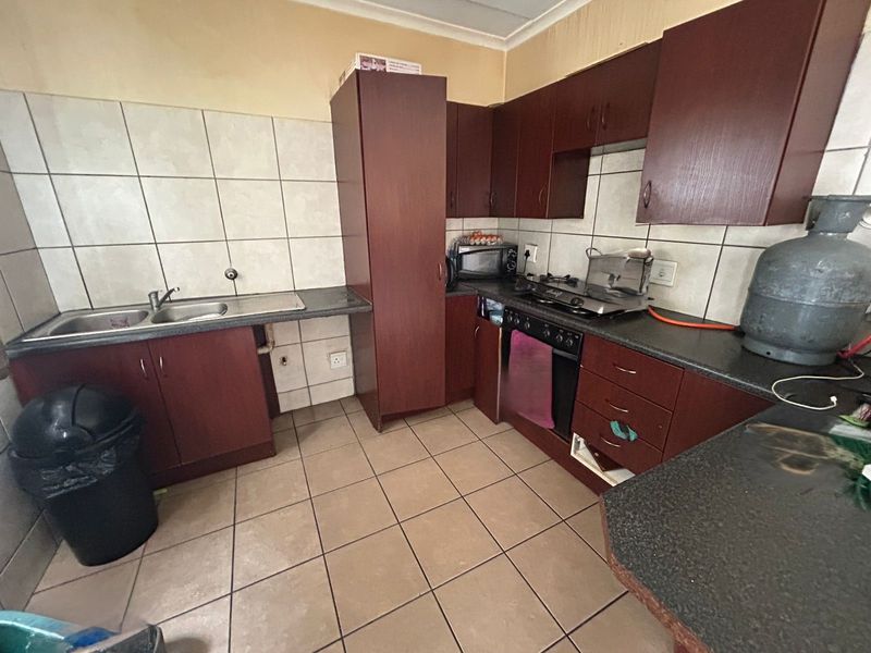 A functional kitchen featuring dark laminate cabinetry, tiled backsplash, built-in oven with gas hob, and ceramic floor tiles, offering potential for modern cosmetic updates.