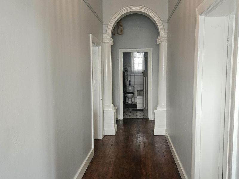 A bright hallway featuring original hardwood flooring, a classic architectural archway with decorative columns, and high ceilings.