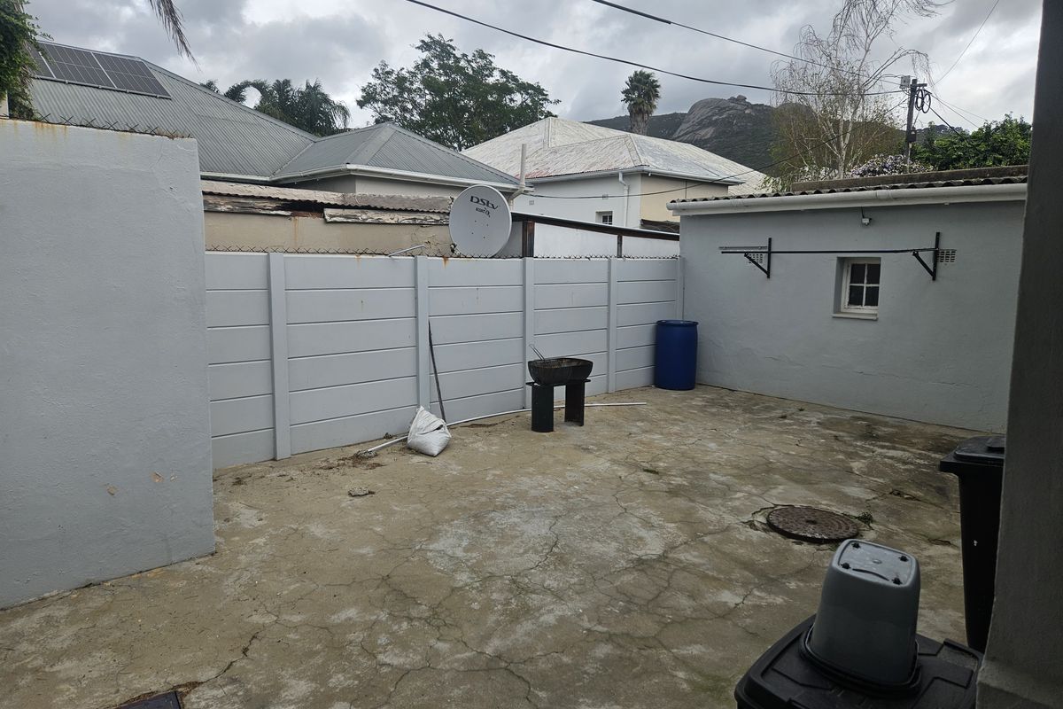 A rear courtyard area featuring a precast concrete boundary wall, concrete paving, and wall-mounted washing line, offering potential for outdoor improvement.