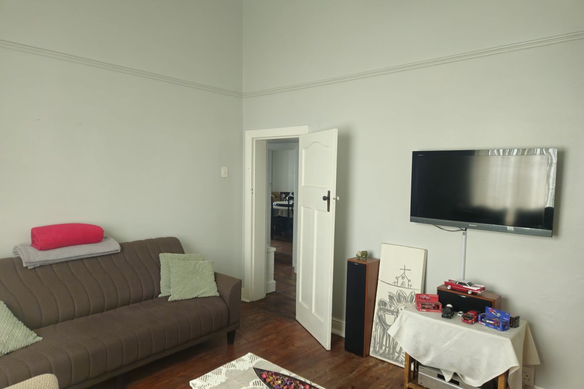 A living room featuring hardwood flooring, high ceilings with picture rails, and a neutral wall finish.