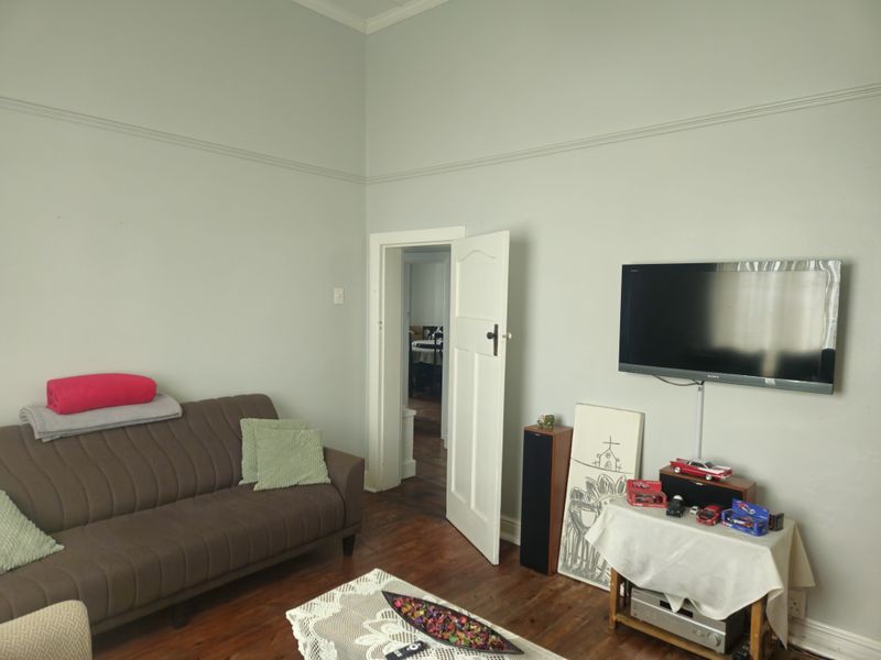 A living room featuring hardwood flooring, high ceilings with picture rails, and a neutral wall finish.