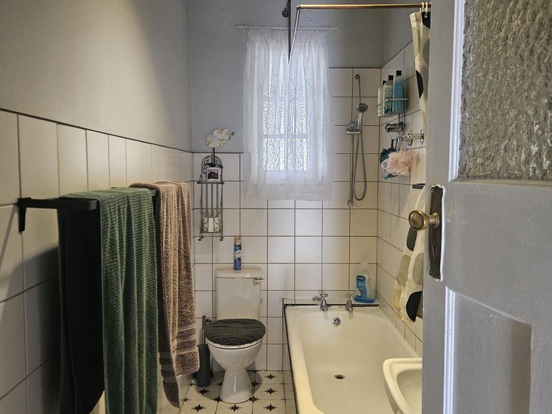 A functional bathroom featuring a bathtub with shower mixer, toilet, basin, and classic white wall tiling with patterned floor tiles.