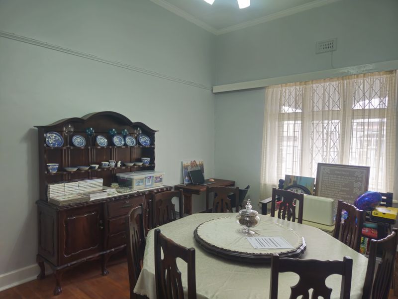 A dining room featuring timber flooring, classic picture rails, and a large window with security gate, offering a traditional and functional living space.