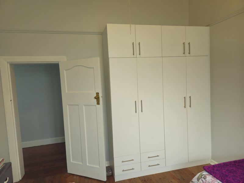 A bedroom featuring polished timber flooring, a built-in wardrobe with overhead storage, and classic picture rail detailing.