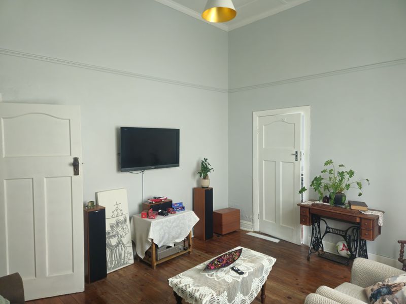 A living room featuring original hardwood flooring, classic panelled doors, and decorative picture rails, offering a character-filled space with potential for modern updates.