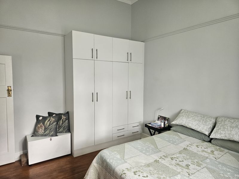 A well-maintained bedroom featuring classic hardwood flooring, a built-in white wardrobe with overhead storage, and traditional picture rail detailing.