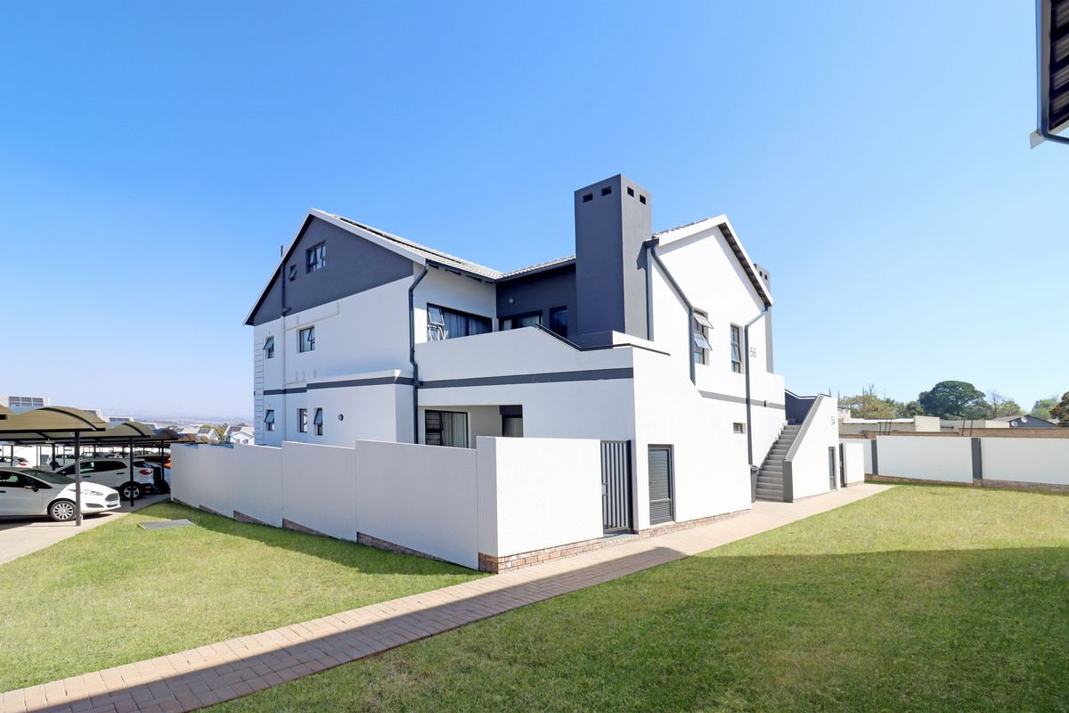 Rear view of a modern townhouse featuring a clean white and grey facade, a chimney, an external staircase, and a well-maintained lawn.