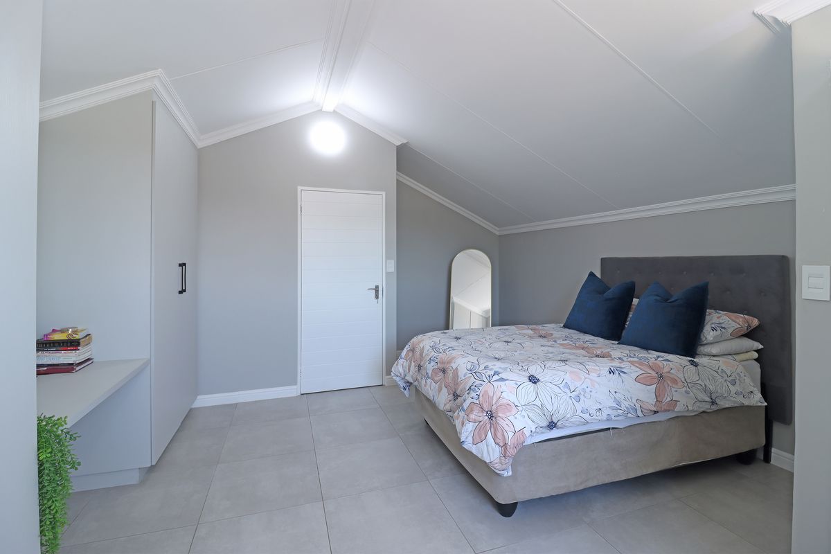 A well-maintained bedroom featuring vaulted ceilings, crown molding, tiled flooring, and built-in cupboards, offering a clean and modern aesthetic.