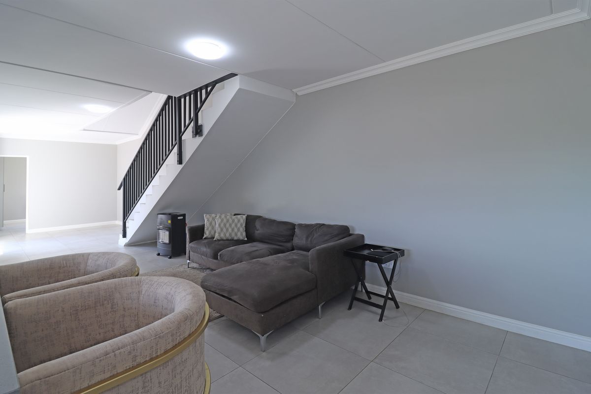 Spacious living area featuring neutral tiled flooring, a staircase with a dark railing, and clean, modern finishes throughout.