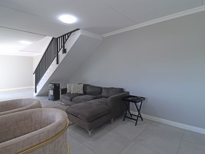 Spacious living area featuring neutral tiled flooring, a staircase with a dark railing, and clean, modern finishes throughout.
