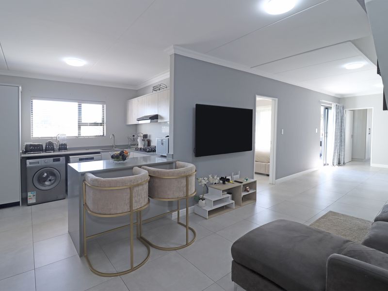 Modern open-plan living area featuring a sleek kitchen with island, tiled flooring, and neutral grey walls, seamlessly connecting to the lounge space.