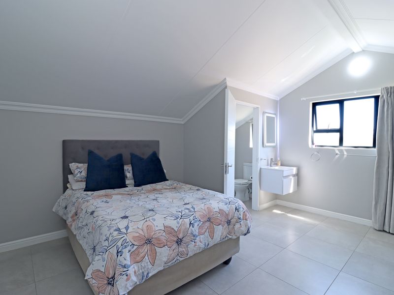 A well-maintained bedroom featuring a vaulted ceiling, neutral tiled flooring, and an adjoining en-suite bathroom with a modern wall-mounted vanity.