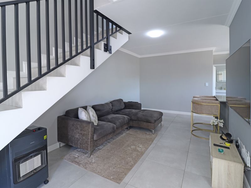 A modern living area featuring tiled flooring, a staircase with a black metal balustrade, and neutral wall finishes.