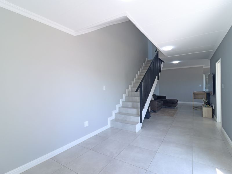 A bright, open-plan living area featuring neutral grey walls, large format floor tiles, and a modern staircase with a black metal balustrade.