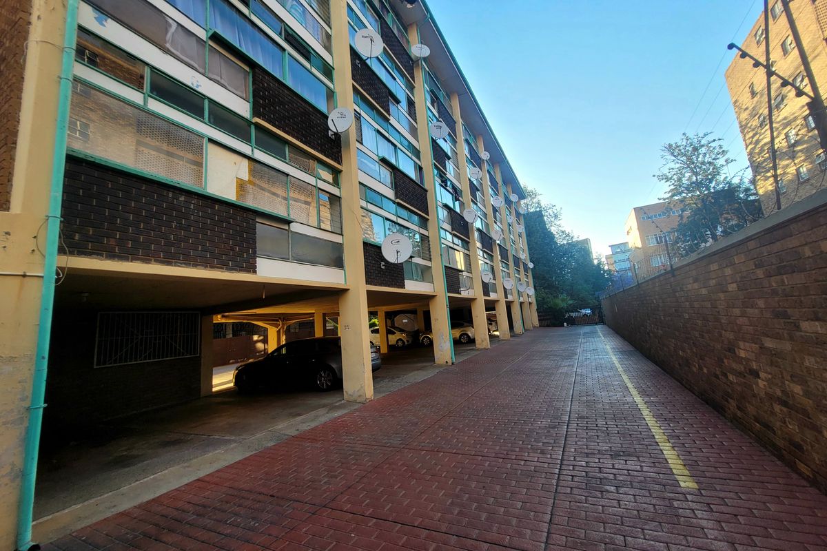 Rear exterior view of the apartment building featuring covered parking bays, brick paving, and a perimeter boundary wall.