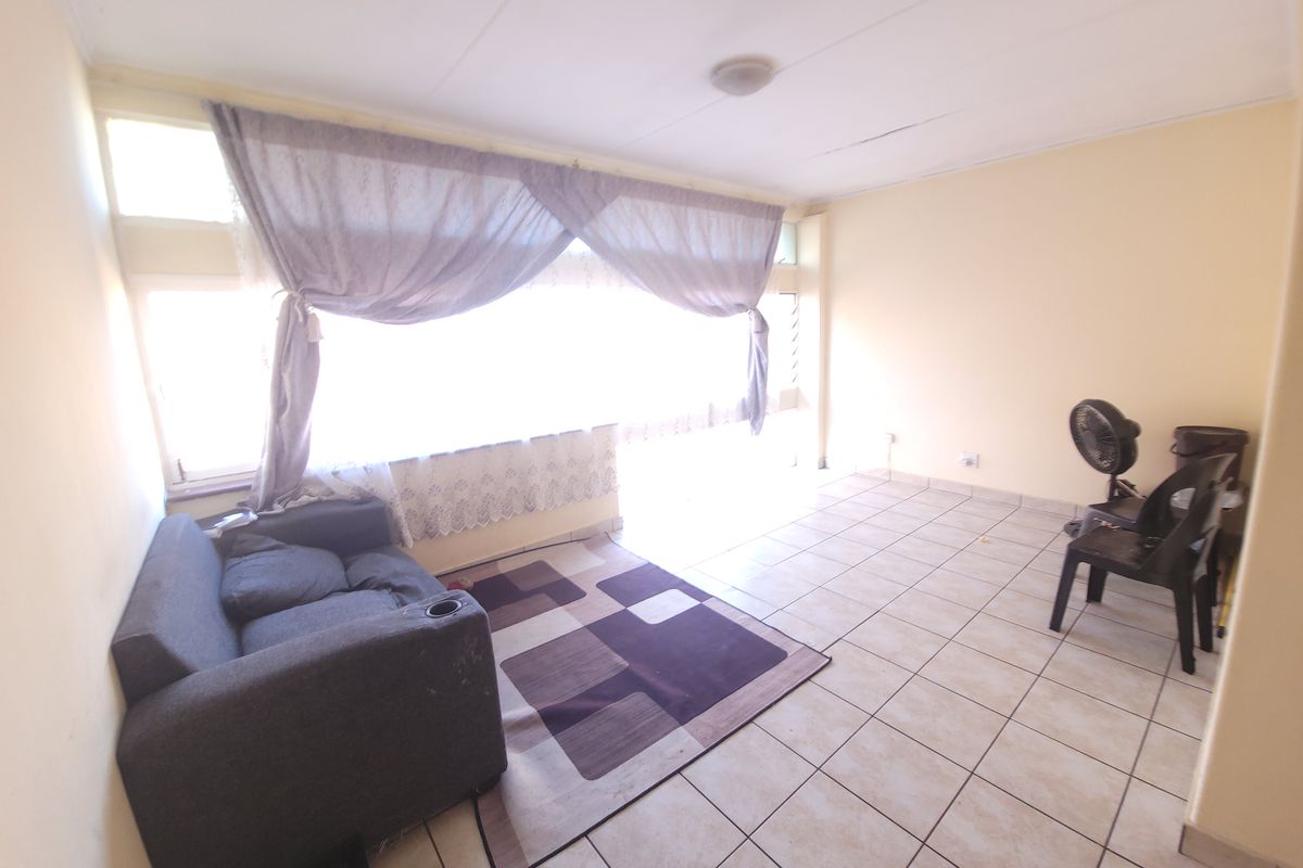 A living room featuring tiled flooring and a large window, currently in need of cosmetic updates and ceiling repairs.