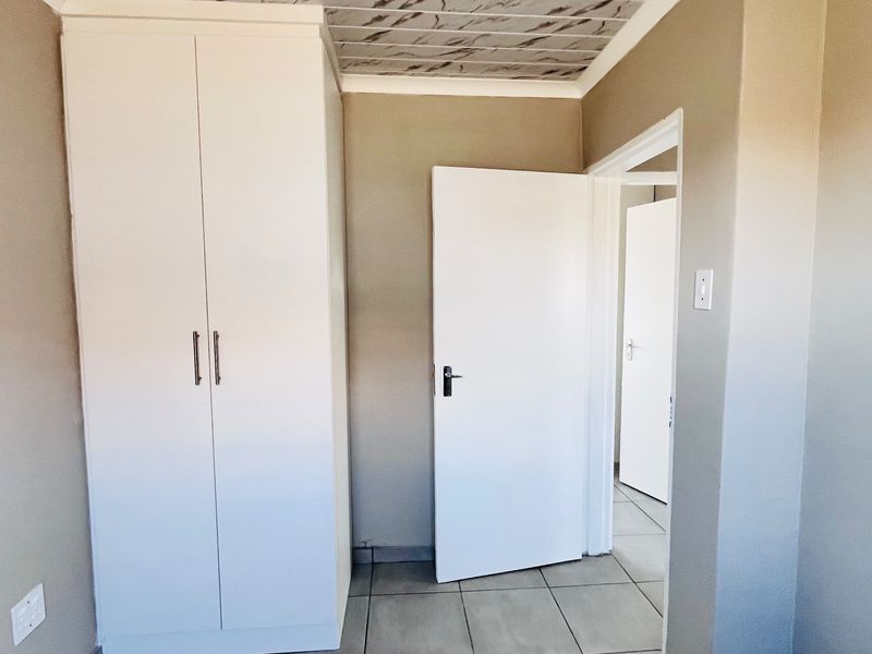 A clean, empty bedroom featuring built-in wardrobes, tiled flooring, and a unique patterned ceiling finish.