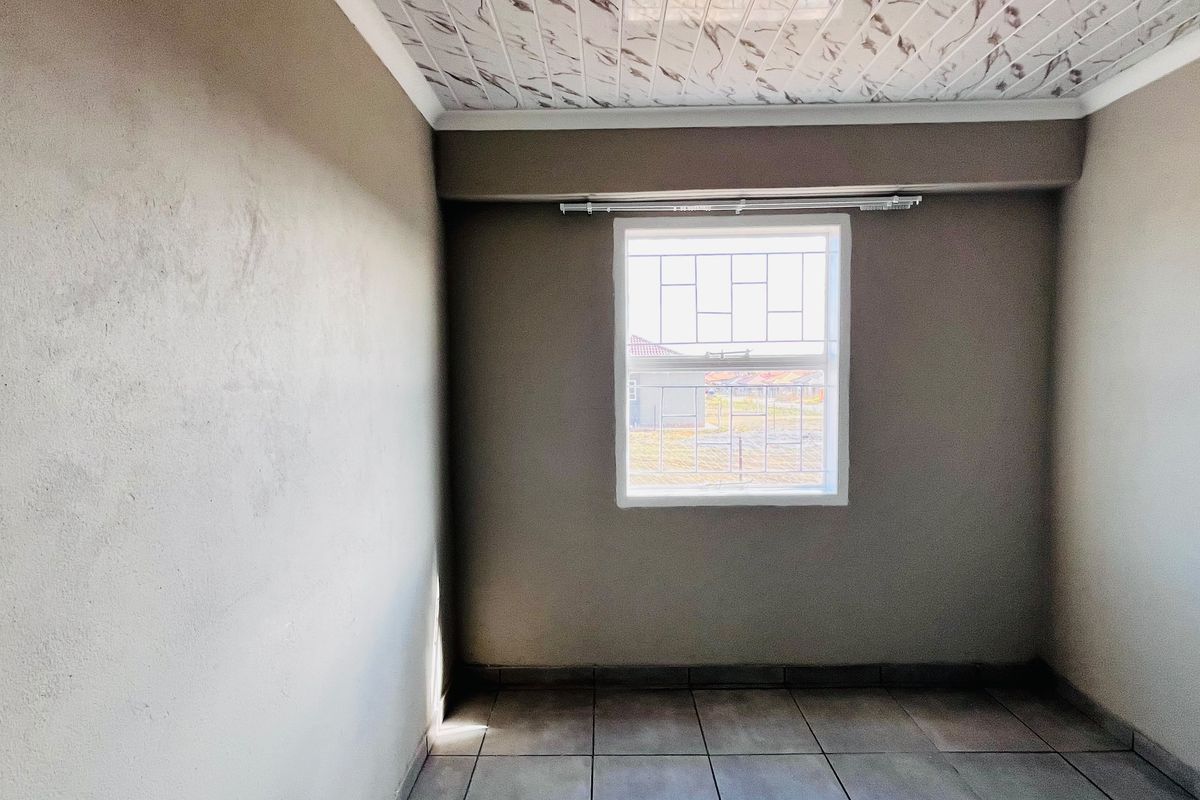 An empty bedroom featuring tiled flooring, decorative ceiling panels, and a window fitted with security bars.