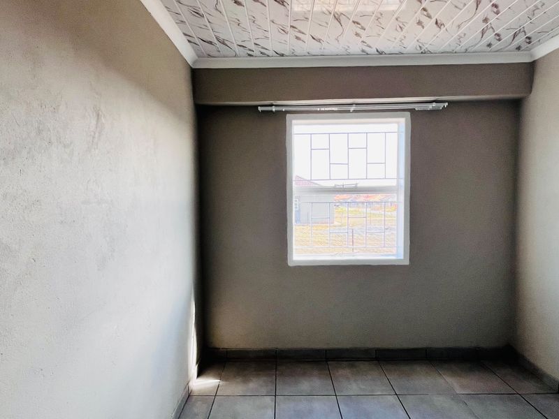 An empty bedroom featuring tiled flooring, decorative ceiling panels, and a window fitted with security bars.