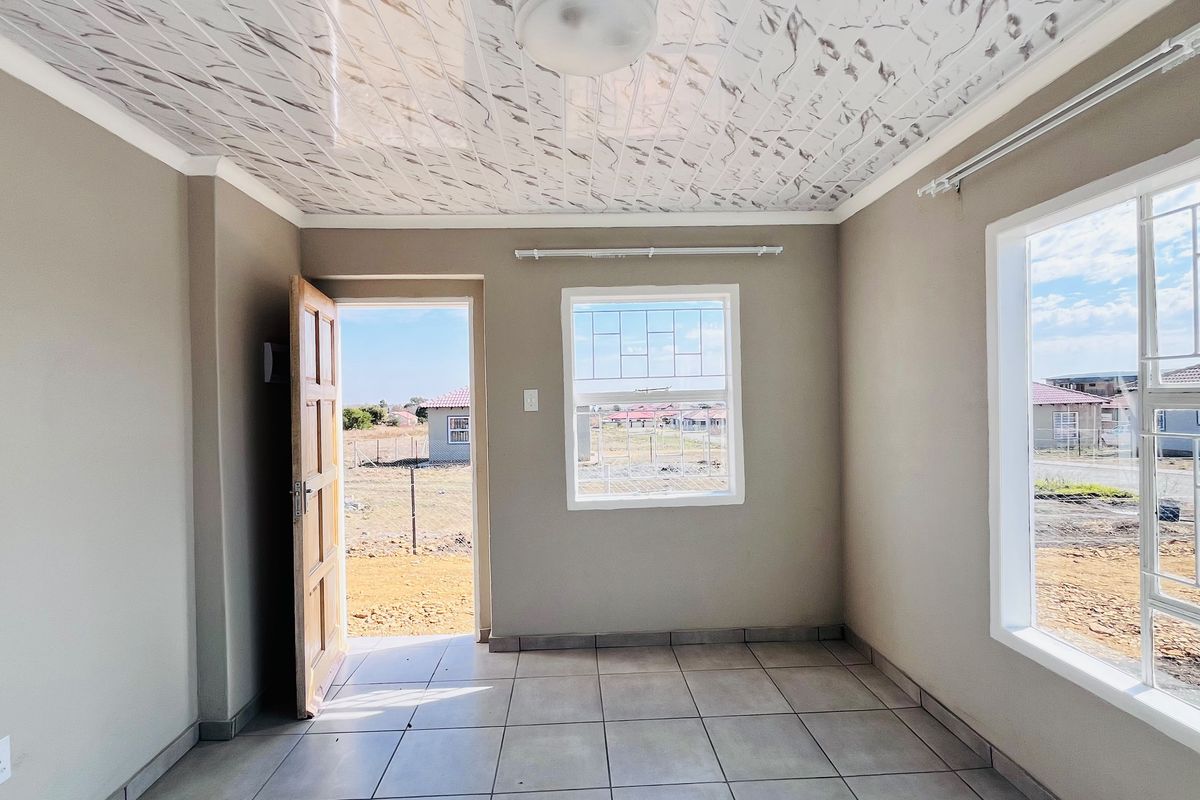 A bright, empty living area featuring tiled floors, decorative ceiling panels, and security bars on the windows, with direct access to the exterior.