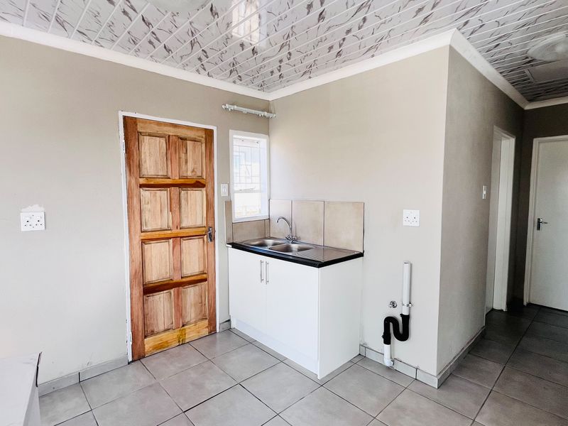 A functional scullery area featuring a stainless steel sink, built-in white cabinetry, tiled flooring, and a decorative PVC ceiling.