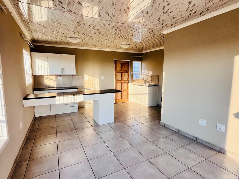 An open-plan kitchen and living area featuring tiled floors, built-in cabinetry with laminate countertops, and decorative ceiling tiles.