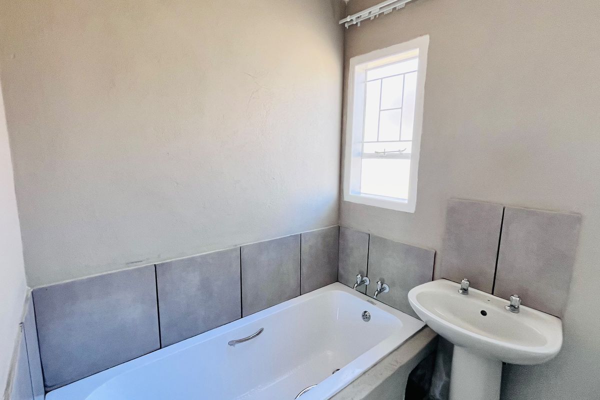 A clean, functional bathroom featuring a white bathtub, pedestal basin, and neutral wall tiles, offering a simple and practical layout.