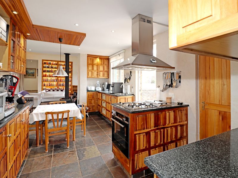 Open-plan kitchen and living area featuring extensive wooden cabinetry, granite countertops, a central gas hob, and slate tile flooring with a cozy fireplace.