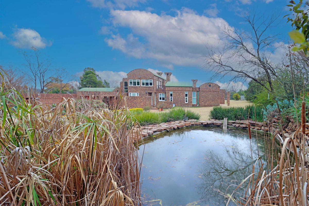 A rear view of a unique brick house featuring a natural pond, landscaped garden, and architectural detailing under a clear blue sky.