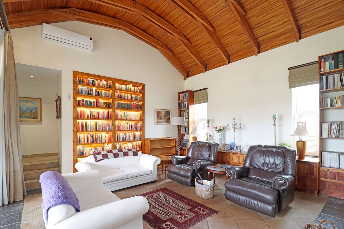 Spacious living room featuring a striking vaulted timber ceiling, tiled flooring, and a large built-in illuminated bookshelf.