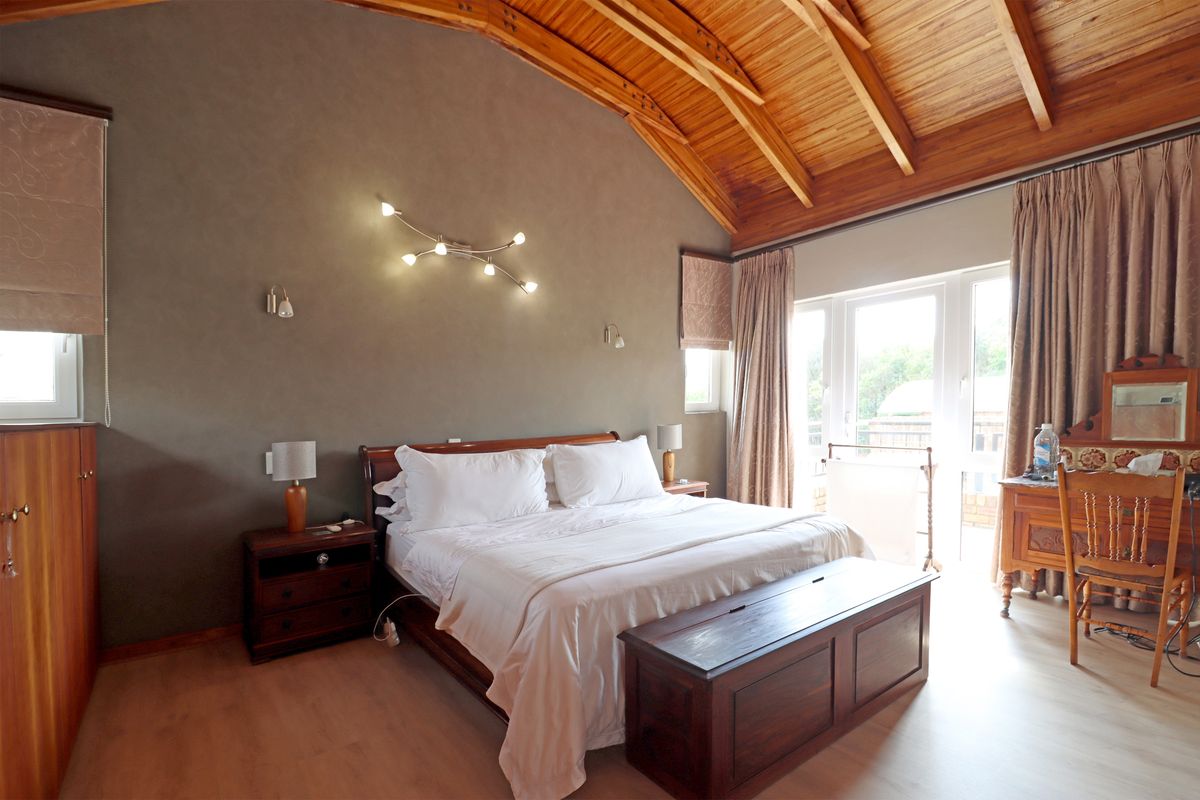 Spacious bedroom featuring a high vaulted timber ceiling, laminate flooring, and direct access to the outdoors through glass french doors.