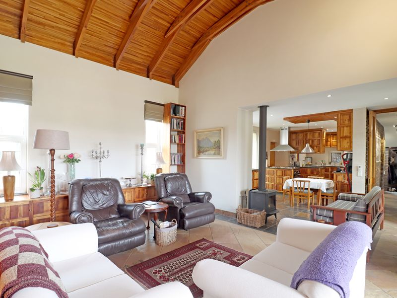 Spacious open-plan living area featuring a vaulted timber ceiling, tiled floors, and a central wood-burning fireplace, seamlessly connecting to the kitchen and dining space.