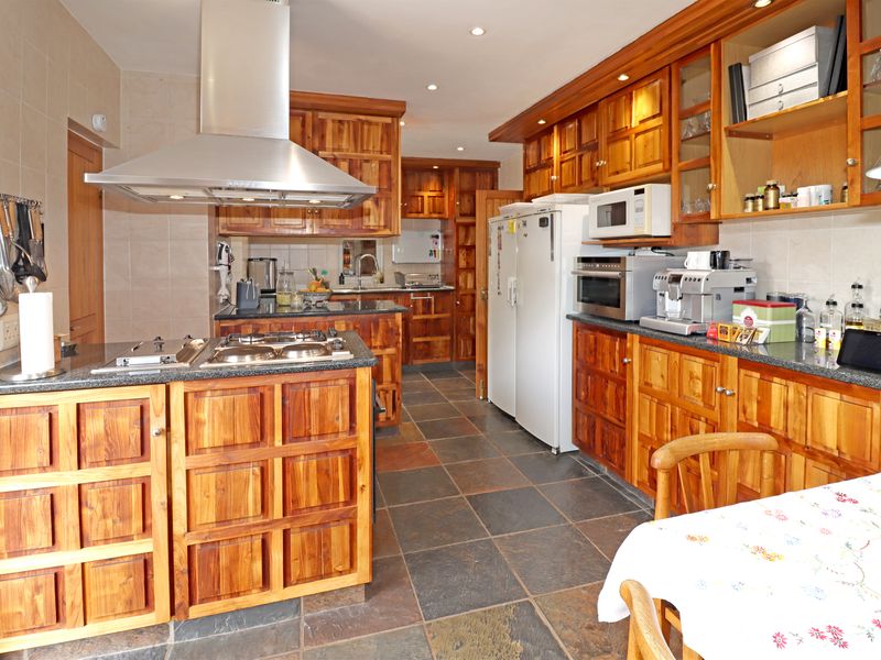 Spacious kitchen featuring extensive wooden cabinetry, granite countertops, a central island with a gas hob, and durable slate tile flooring.