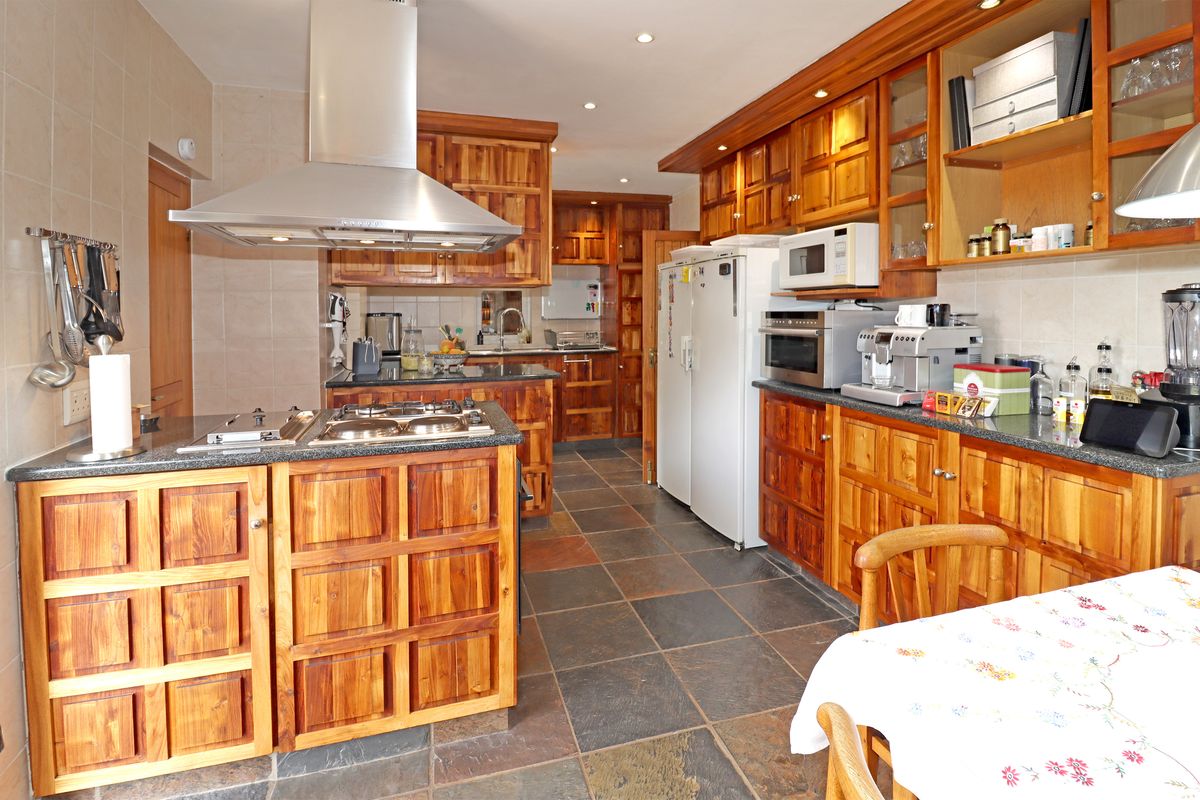 Spacious kitchen featuring extensive wooden cabinetry, granite countertops, a central island with a gas hob, and durable slate tile flooring.