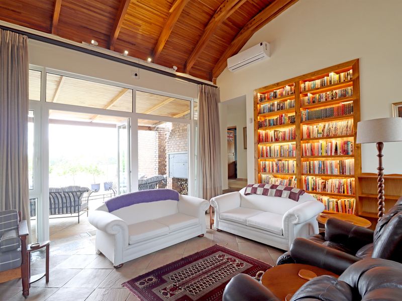 Spacious living room featuring a vaulted timber ceiling, built-in illuminated bookshelf, and large glass doors providing seamless access to the outdoor patio area.