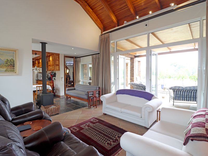 Spacious open-plan living area featuring a vaulted timber ceiling, a central fireplace, and large glass doors opening onto a covered patio.