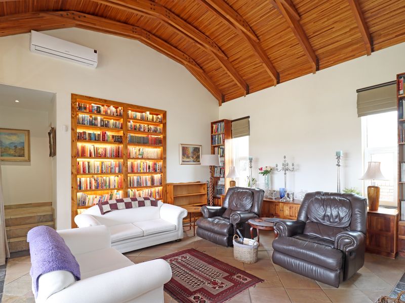Spacious living room featuring a striking vaulted timber ceiling, tiled flooring, and a large built-in illuminated bookshelf.
