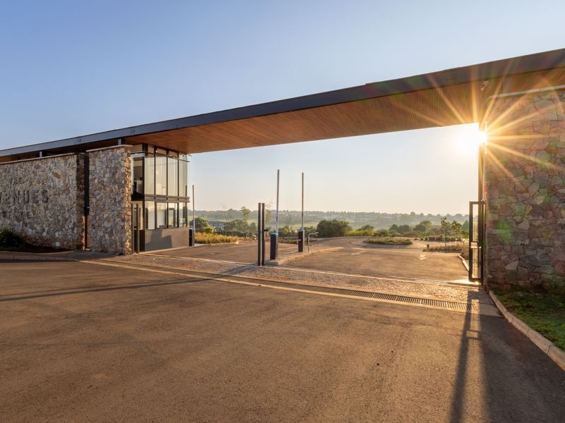 A modern, well-maintained security entrance gatehouse featuring stone cladding, a timber soffit, and automated boom gates at the estate approach.