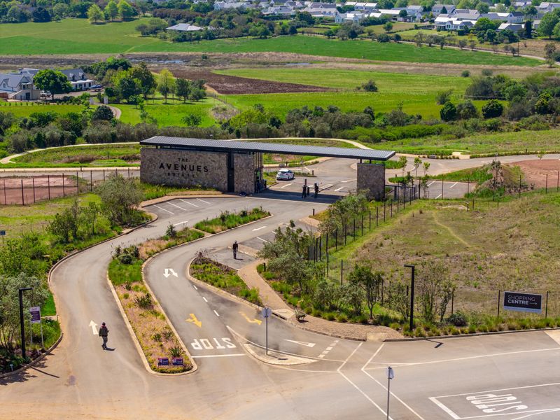 Aerial view of The Avenues Estate entrance, featuring a modern stone-clad security gatehouse, paved access roads, and landscaped surroundings.