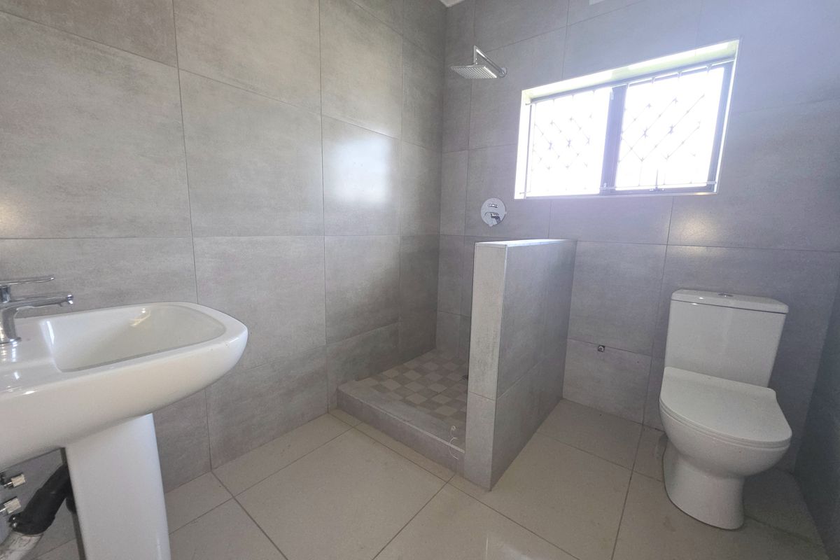 A modern bathroom featuring large-format grey wall tiles, a walk-in shower, a pedestal basin, and a toilet.