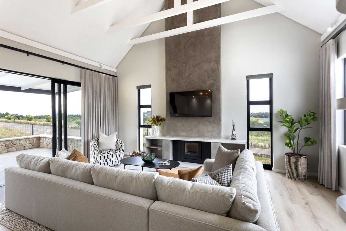 Spacious living room featuring a vaulted ceiling, exposed beams, and a modern fireplace with a feature chimney breast, opening onto a covered patio.