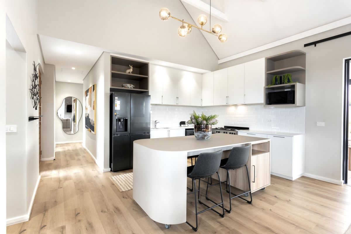 Modern open-plan kitchen featuring sleek white cabinetry, subway tile backsplash, a central island with integrated seating, and high vaulted ceilings.