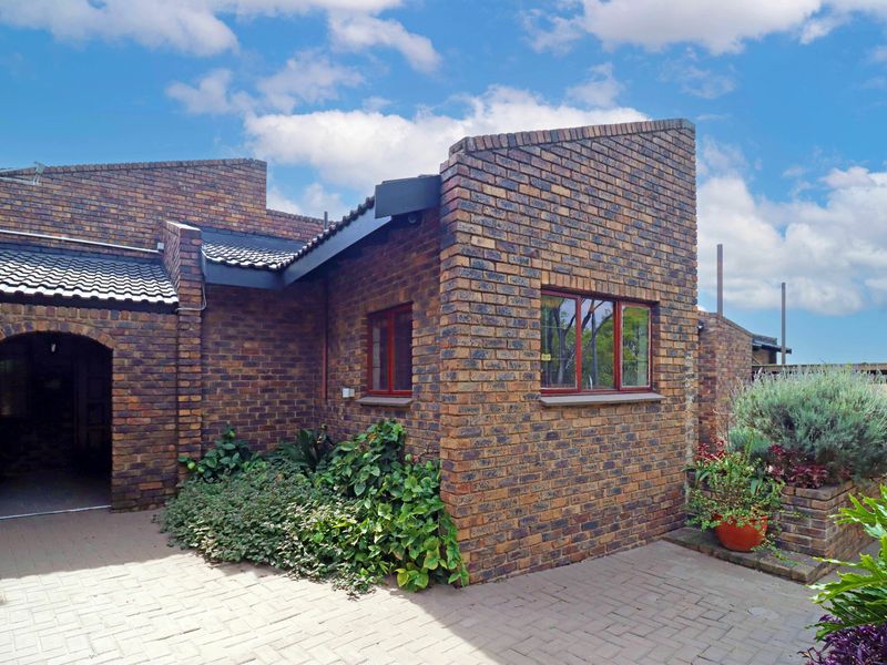 A well-maintained rear exterior view featuring a face brick facade, tiled roof, and a paved patio area with integrated brick planters.