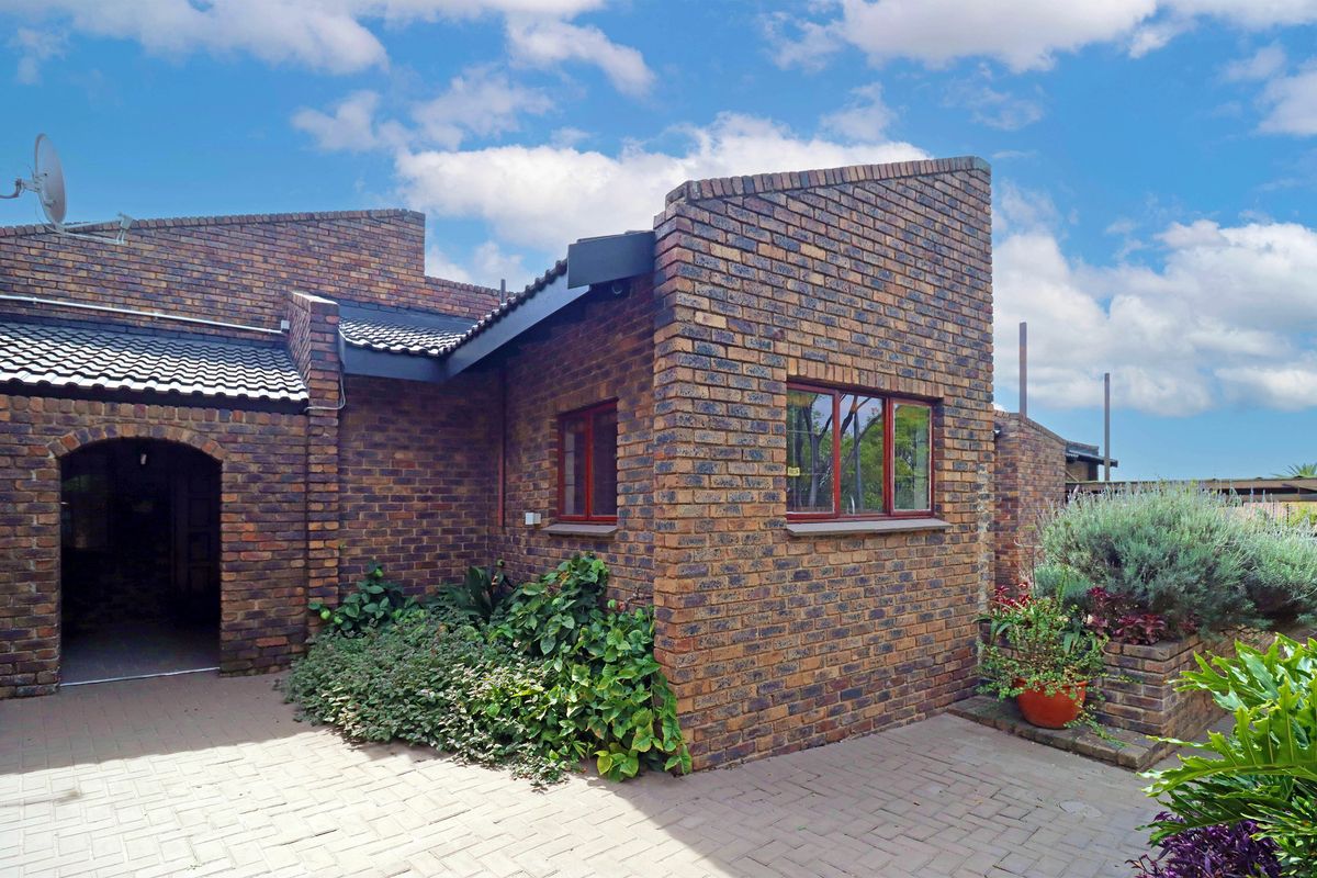 A well-maintained rear exterior view featuring a face brick facade, tiled roof, and a paved patio area with integrated brick planters.
