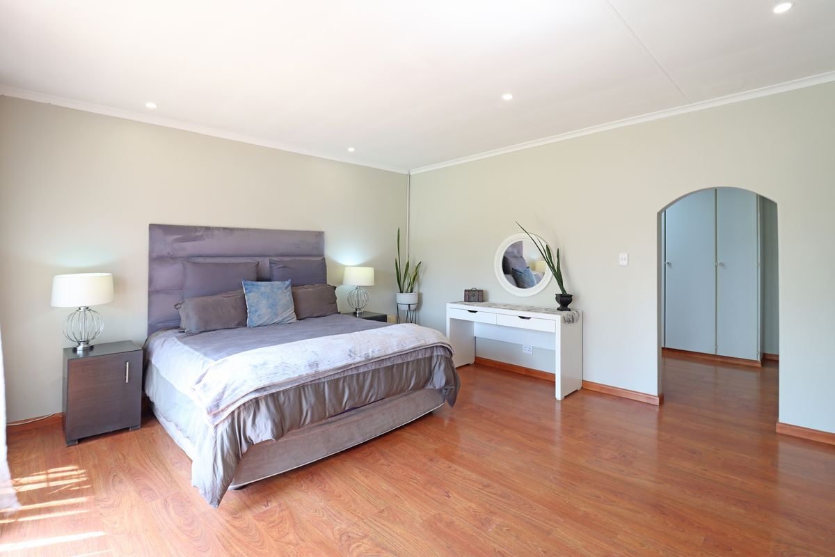 Spacious bedroom featuring warm laminate flooring, recessed downlighting, and a classic arched entryway leading to a dressing area with built-in cupboards.